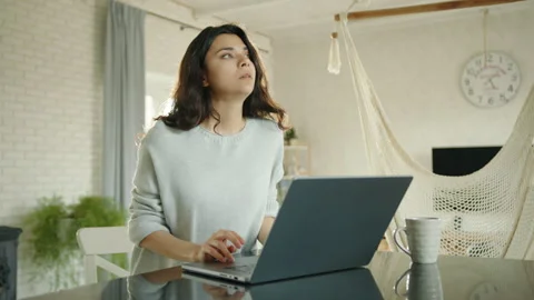 Sad cute brunette typing on silver laptop sitting at table in living room Video stock 244326488