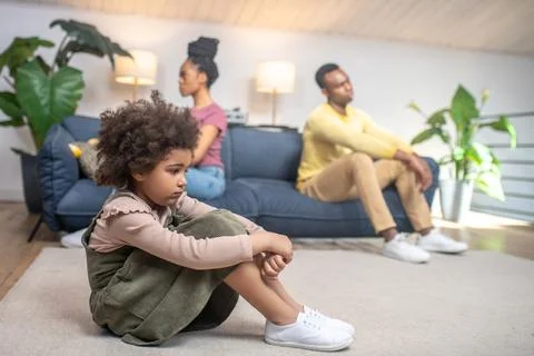Sad daughter on floor and unhappy parents on couch Stock Photos