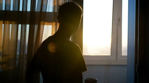 A sad, depressed man is drinking tea at the window of his apartment during a Stock Footage 169629980