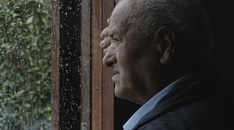Sad depressed old man looking outside the window during a rainstorm: lonely man Video stock 68750082