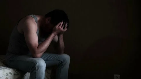 Sad depressive pensive caucasian man 40 years old sitting on bed in dark room Stock Footage 130564458