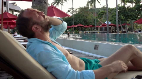 Sad, desperate man sitting on sunbed by swimming pool Stock Footage 59141417