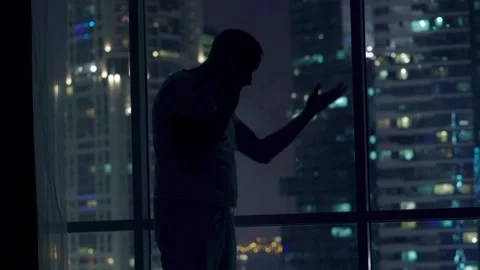 Sad, desperate man talking on cellphone standing by window during night Stock Footage 103260154