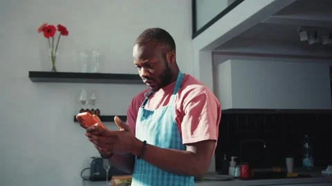 Sad downhearted black man in apron reading negative news on mobile phone Stock Footage 131669818