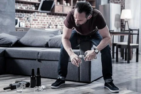 Sad drunk man looking at empty bottles Stock Photos