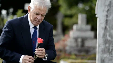 Sad elderly man lays flower on grave, looks at headstone Stock Footage