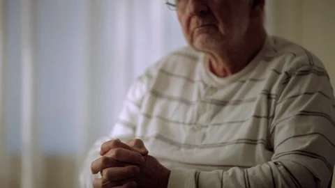 Sad elderly man in a rest home looks up from his anxiously clasped hands. Vidéo 88342289