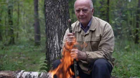 A sad elderly man is sitting in the forest by the fire warming himself in the Stock-Footage 159549125