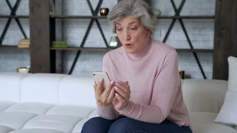 Sad elderly woman sit on sofa hold smartphone feels disappointed by received sms Stock Footage 137586816