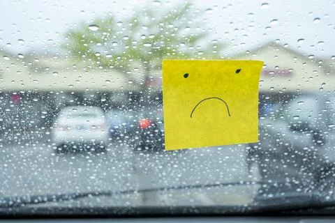 Sad face sticky note on a rainy car windshield Foto stock