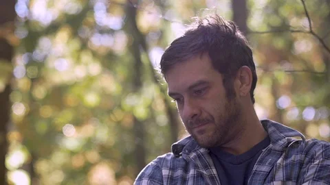 Sad, frustrated handsome man thinking and looking down in the woods Video stock 98434541