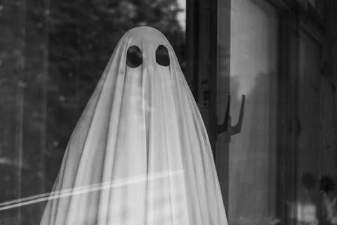 Sad ghost in white sheet outside the window of an abandoned house 写真素材
