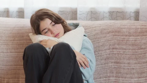 A sad girl is crying while sitting on the couch, clutching a pillow to herself.  Stock Footage 170616977