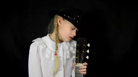 Sad girl holding a guitar and wearing a white dress on a black background Stock Footage 59459012