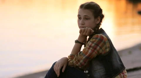 Sad girl thinking silhouette while sitting by the lake at sunset Stock Footage 65796918