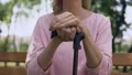 Sad grandmother leaning on walking stick sitting on bench in park, nursing home HD Footage