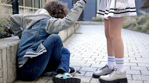Sad guy high school student sits on the sidewalk in the schoolyard and waits for Stock Footage 220443101