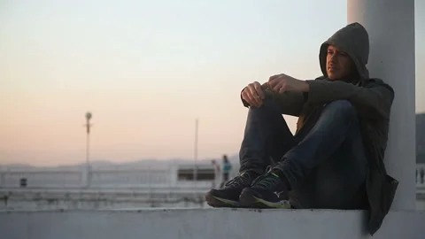 A sad guy in a hooded jacket smokes on the embankment Vidéo 150250648