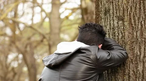 Sad guy at park strikes the tree with a punch Stock Footage 10582367