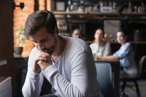 Sad guy sitting alone separately from other mates in cafe Foto stock