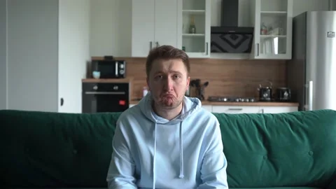 Sad guy sitting on the couch in the living room, looking at the camera Stock Footage 155679504