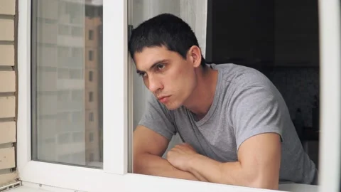 Sad guy standing window. Depression and problems during period quarantine Stock Footage 130956953