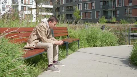 A sad guy is texting on the phone, sitting on a bench near the house Stock Footage 160345235