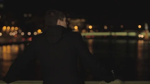 Sad handsome man with beard and brown hair leaning on a railing of the bridge, 動画素材 110914323