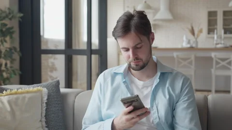 Sad Handsome Man Using Mobile Phone Lying on Cozy Sofa in Living Room at Home Stock Footage 299289173