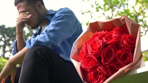 Sad heart broken man sitting on the bench with bouquet of roses at the park Stock Footage 147244944