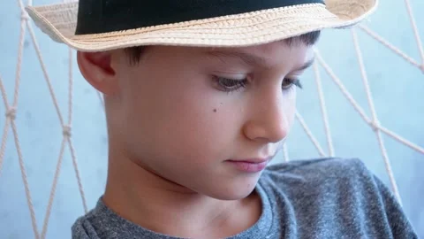 Sad kid with sun fedora hat sitting alone in hammock and thinking about 動画素材 134476537