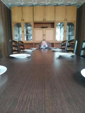 Sad lonely boy sits at an empty huge dining table. loneliness in isolation Stock Photos