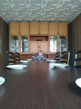 Sad lonely boy sits at an empty huge dining table. loneliness in isolation Stock Photos