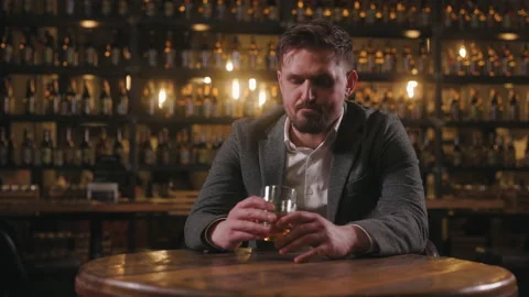 A sad man dressed in a jacket and shirt is sitting in a pub with a glass of Stock Footage 237747958