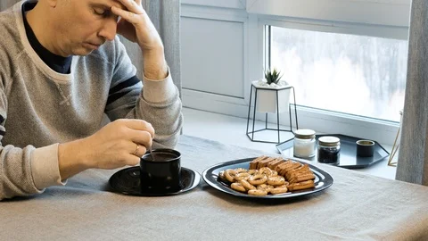 Sad man drinking coffee at the table. Home in his kitchen. He worries because of Stock-Footage 99174229
