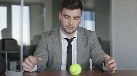 Sad man in a gray jacket ponders future of business rolling a tennis ball. Stock Footage 63884675