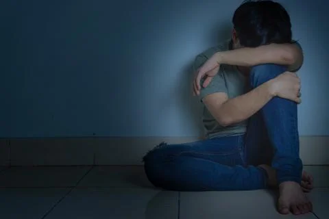 Sad man hug his knee and cry sitting alone in a dark room. Depression, unhapp Stock Photos