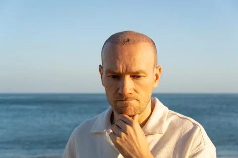 Sad man looking down after hair transplant surgery on beach in Portugal Stock Photos
