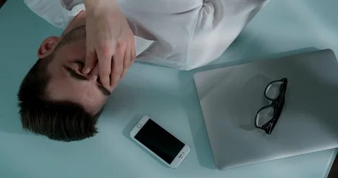 Sad man lying on the table with laptop, smartphone and glasses. He closes his Stock Footage 120512388