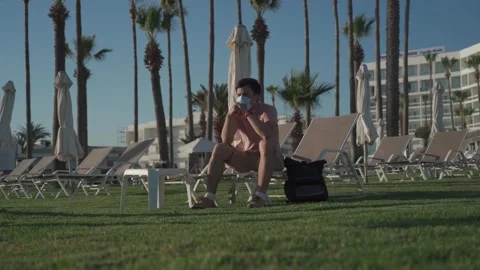 Sad man in protective mask sits on lounger in empty hotel in Cyprus during Stockbeeldmateriaal 166814617