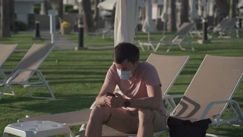 Sad man in protective mask sits on lounger in empty hotel in Cyprus during Stock Footage 166814622