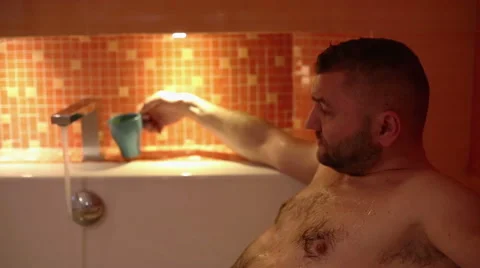 Sad man is seated in bath and drink coffee  Stock Footage 61925754