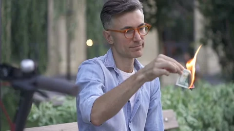 Sad man sitting on the bench and holding burning dollar note.  Stock-Footage 139331300