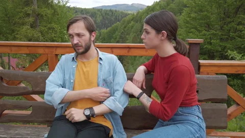 Sad man sitting in a bench in a park.  Woman sits next to man and encourages him Stock-Footage 130545385