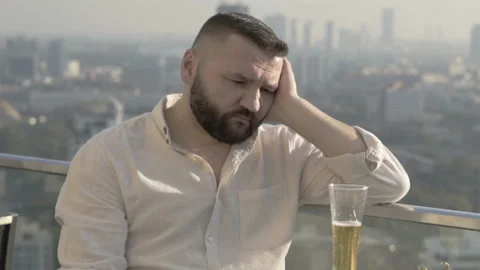 Sad man sitting on the rooftop and drinking beer  Stock Footage 93232382