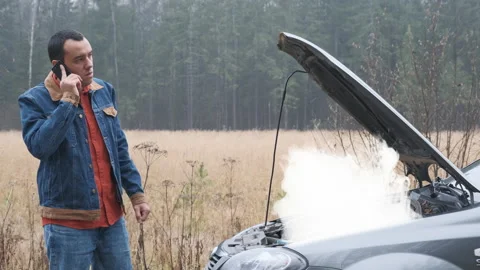Sad man standing on the road by the broken car and calling. Smoke coming out the Stock Footage 144671981