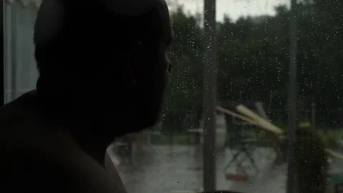 Sad man standing at the window while heavy rain pours outside Stock Footage 324506319