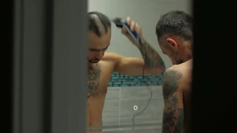 Sad man with tattoos cuts his head in the bath in front of the mirror Stock Footage 144592991