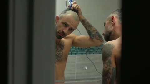 Sad man with tattoos cuts his head in the bath in front of the mirror Stock Footage 144593073