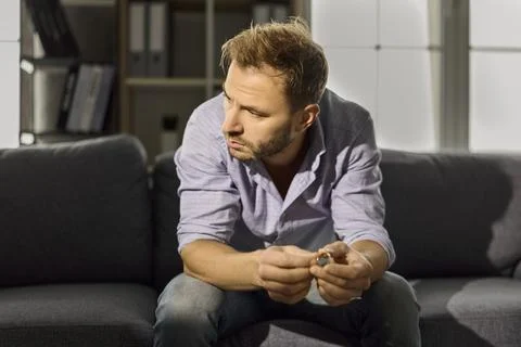 Sad man thinking about divorce and relationship problems, holding wedding ring Stock-Fotos